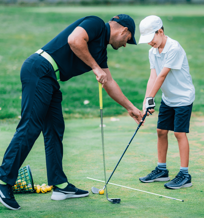 Man teaching a boy how to position the golf club